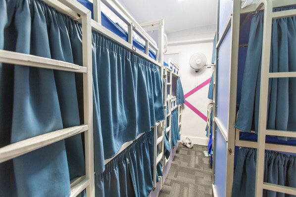 A corridor with bunk beds, each with a curtain.