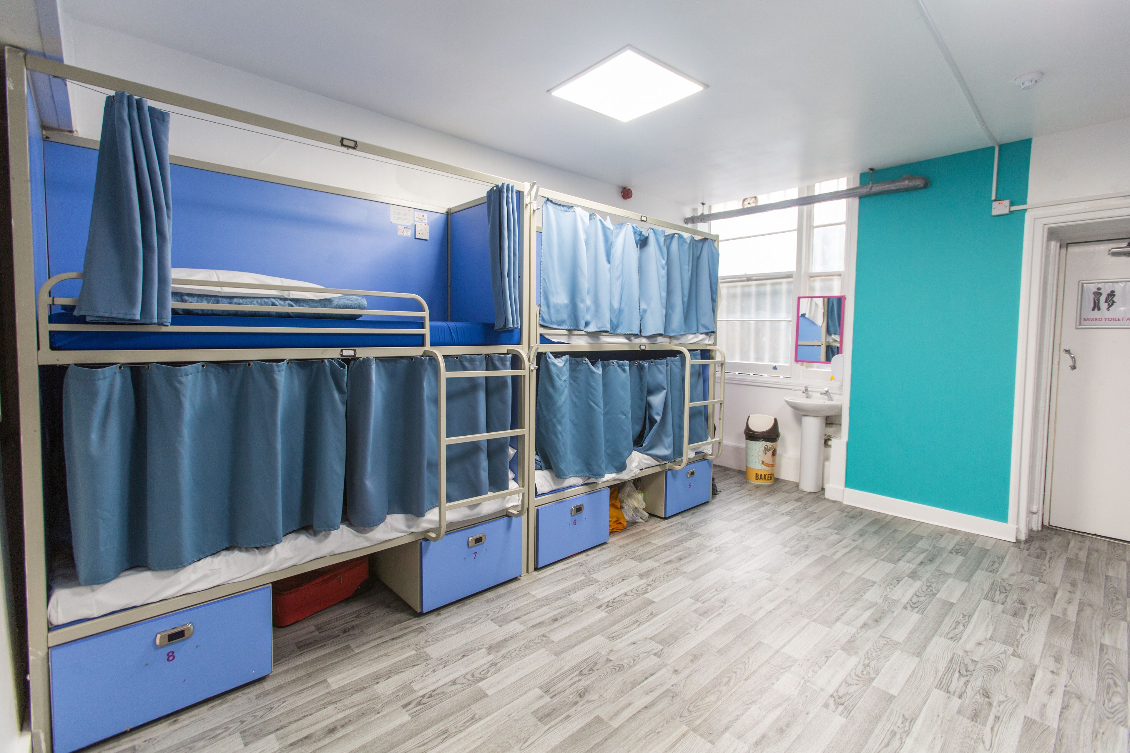 A dormitory room with bunk beds, a sink, and a window.