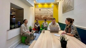 A meeting room with a high ceiling, a skylight, a wooden table, and a green stool.