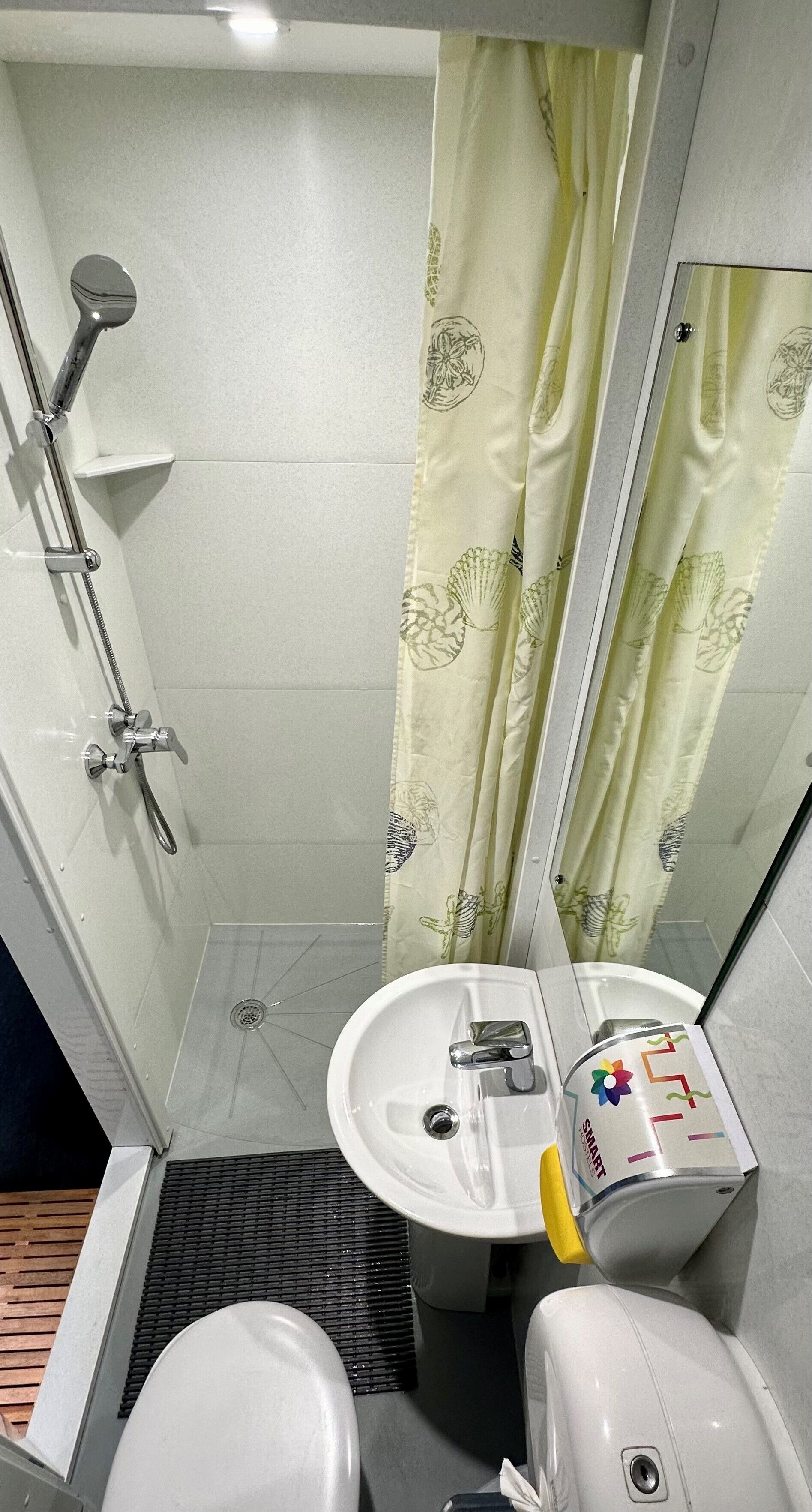 A small bathroom with a shower, toilet, sink, and a mirror.