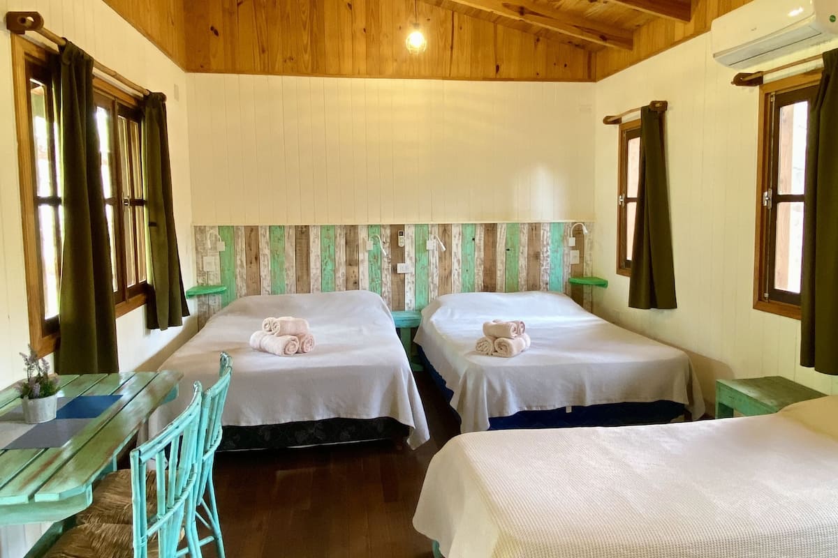 A room with wooden ceiling beams, two beds with white linens, a wooden table with chairs, and a small stool.