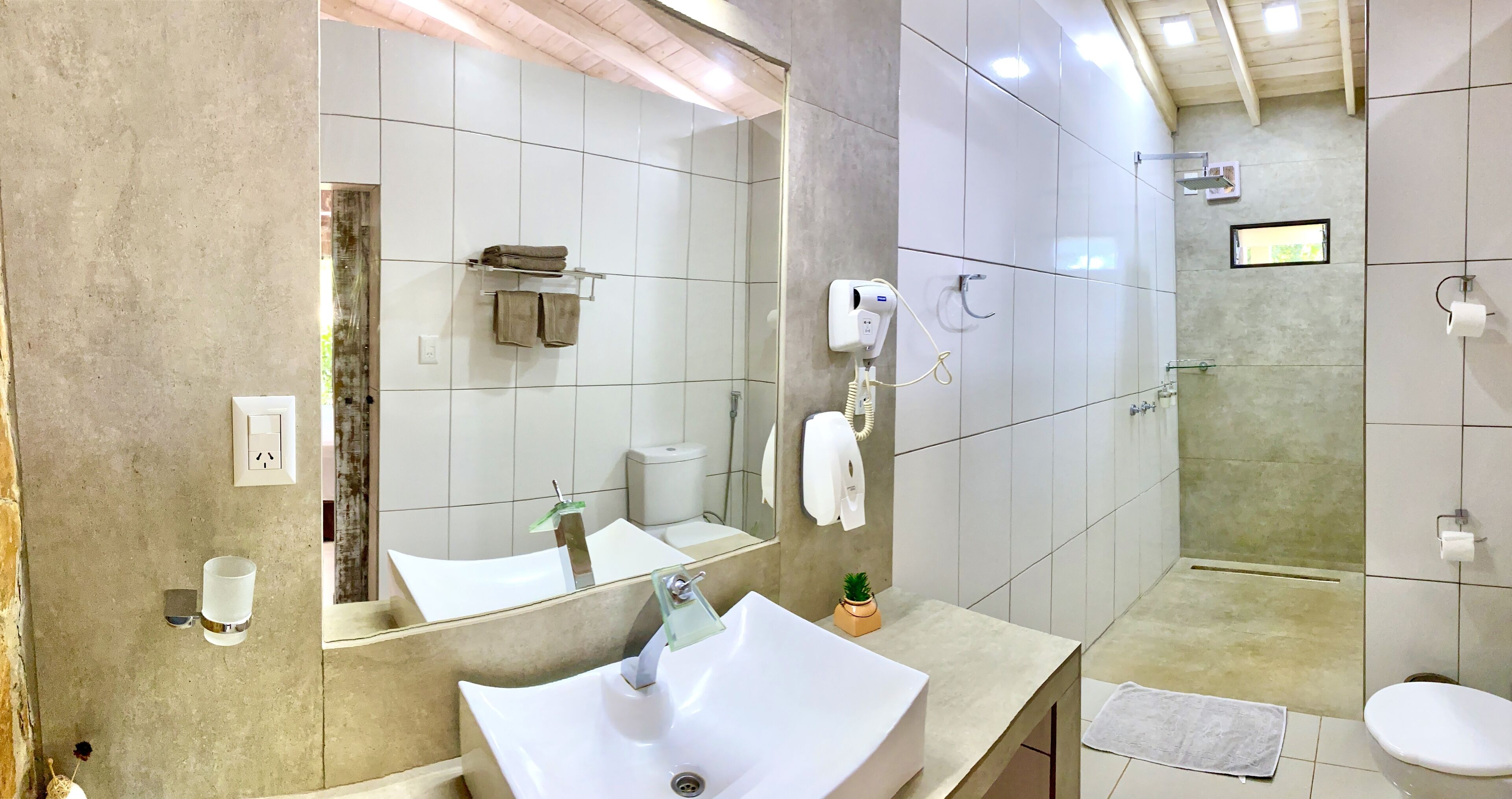 Un baño moderno con un espejo grande, un lavamanos blanco, cabina de ducha con mampara de vidrio y un inodoro.