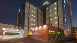 Un hôtel à plusieurs étages, doté d’une enseigne lumineuse, d’une entrée imposante et d’un espace paysager agrémenté de plantes.