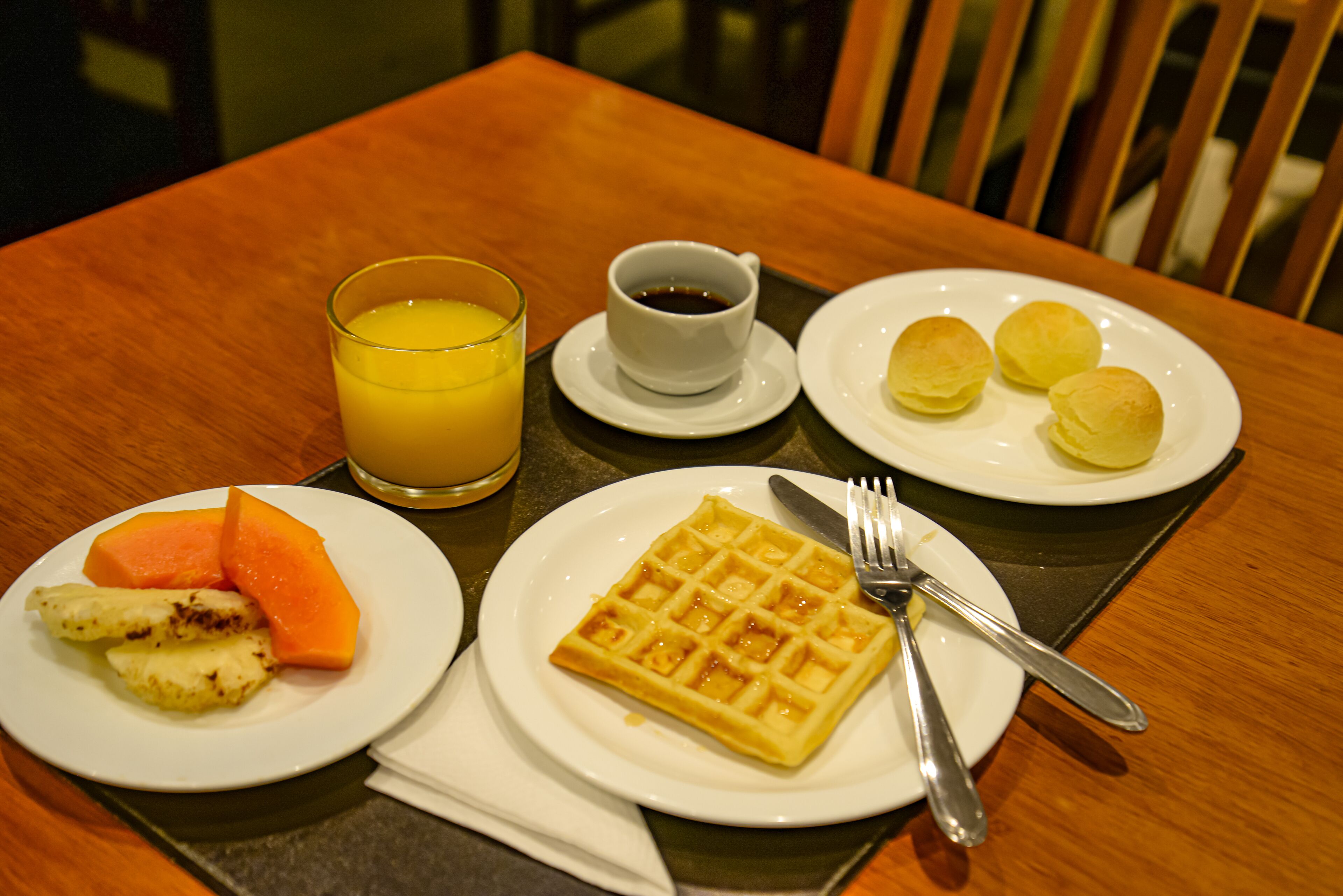 A breakfast setting with a waffle, fruit, juice, and coffee on a wooden table.