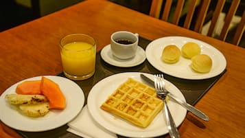A breakfast setting with a waffle, fruit, juice, and coffee on a wooden table.