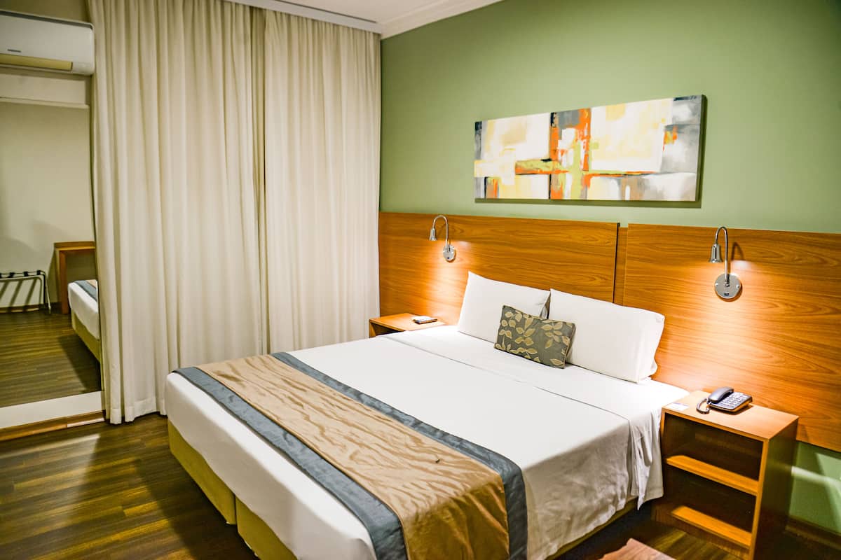 Ein Hotelzimmer mit einem großen Bett, einem Holz-Kopfteil, Nachttischen, einem Telefon und einem Gemälde an der Wand.