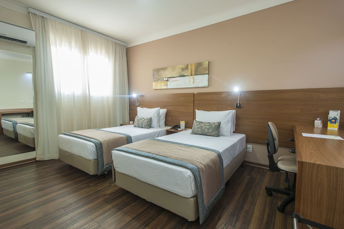 Ein Hotelzimmer mit zwei Betten, einem Holzkopfteil, einem Schreibtisch und einem Stuhl.