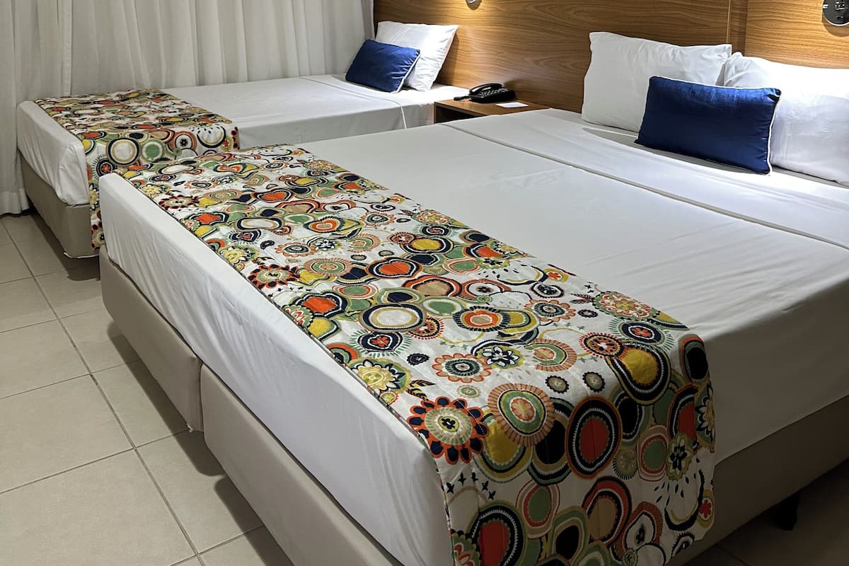 Ein Hotelzimmer mit zwei Betten, jedes mit einer farbenfrohen Tagesdecke, einem Holzkopfteil und einer Wandleuchte.