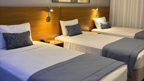 Une chambre d’hôtel avec deux lits, chacun doté d’une tête de lit, de tables de chevet et de lampes. Un tableau est accroché au mur au-dessus des lits, et un appareil de climatisation est fixé au mur.