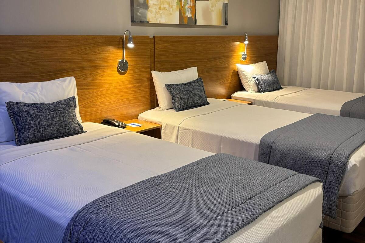 Ein Hotelzimmer mit zwei Betten, jeweils mit Kopfstütze, Nachttischen und Lampen. Darüber hängt ein Gemälde an der Wand und darüber befindet sich eine Klimaanlage.