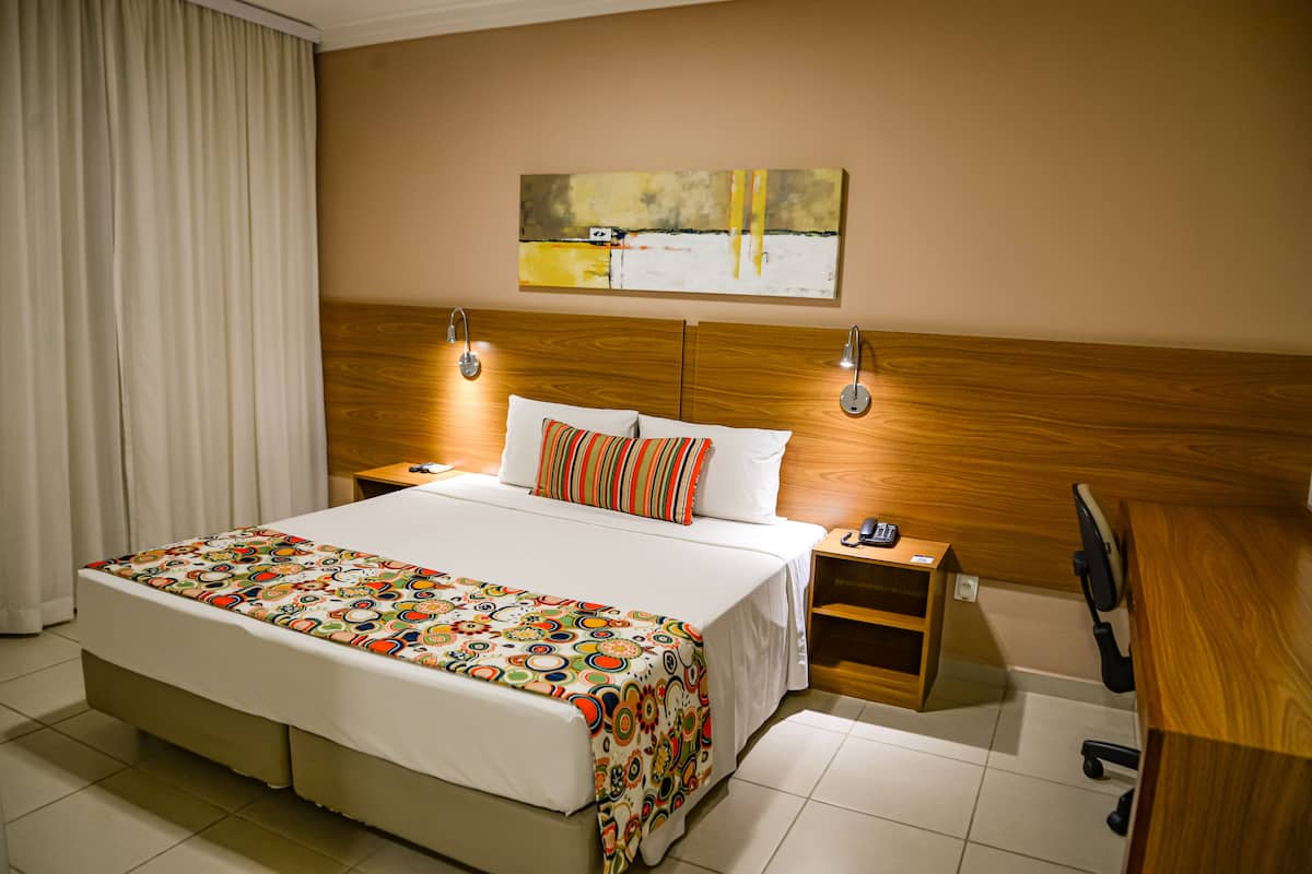 Ein Hotelzimmer mit einem großen Bett, einem Holz-Kopfteil, zwei Nachttischen, einem Schreibtisch und einem Sessel.