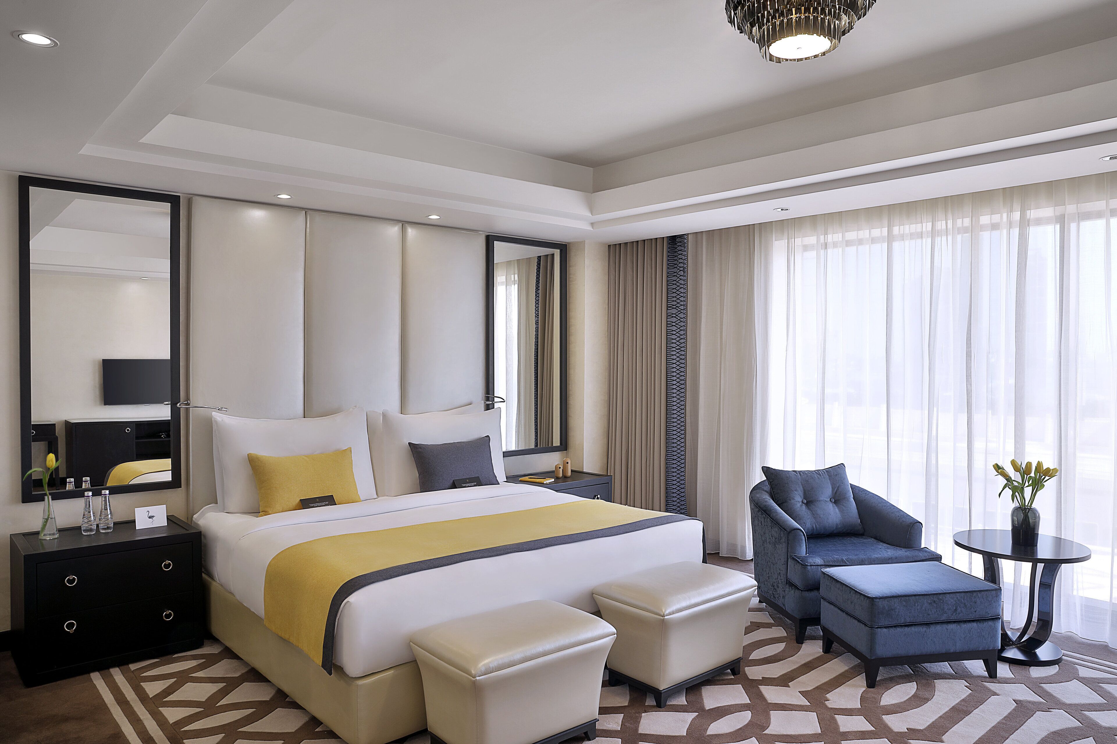 A hotel room with a large bed, two bedside tables, a chair, a small table, and a mirror.