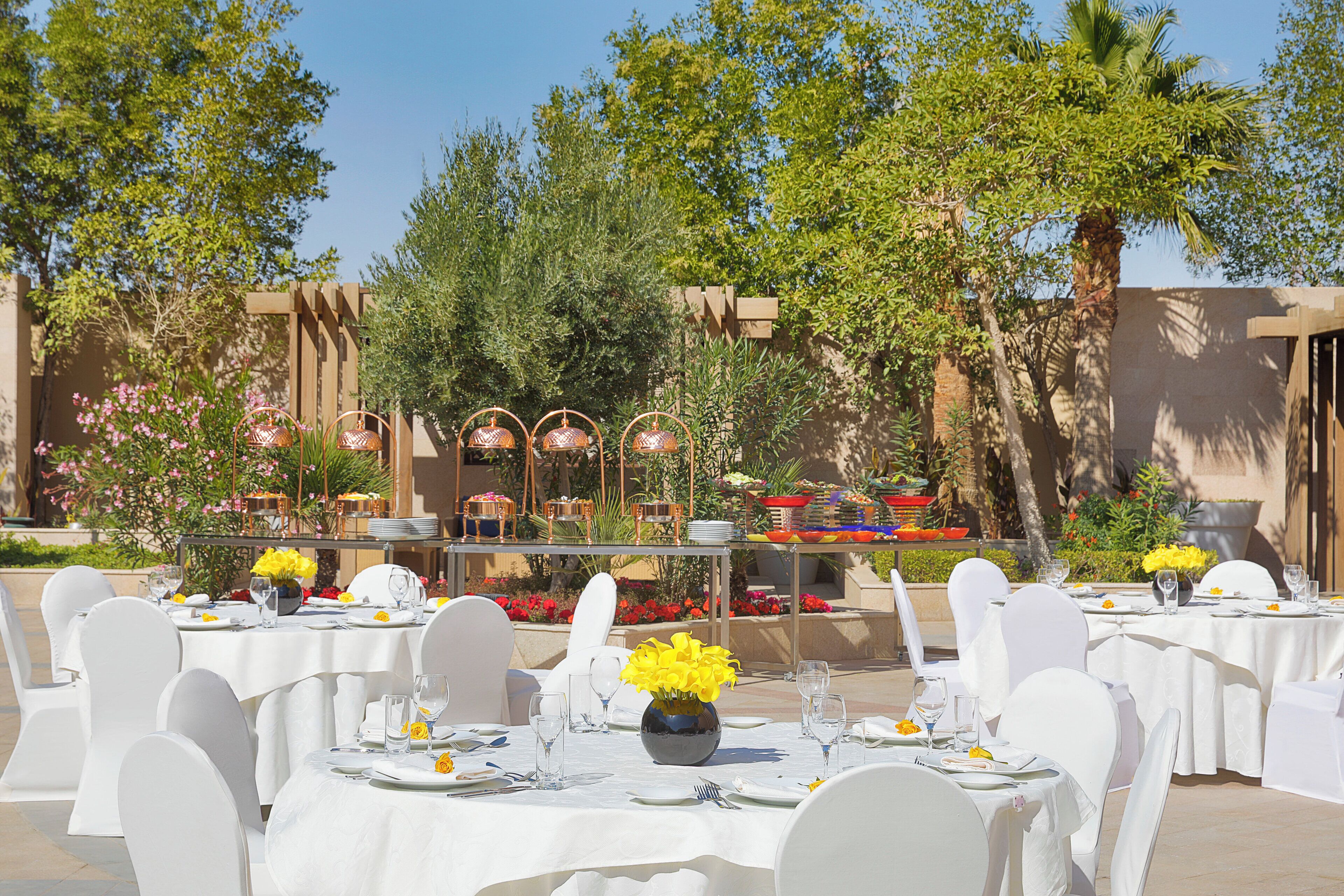 An outdoor dining area with round tables, white chairs, and flower centerpieces.