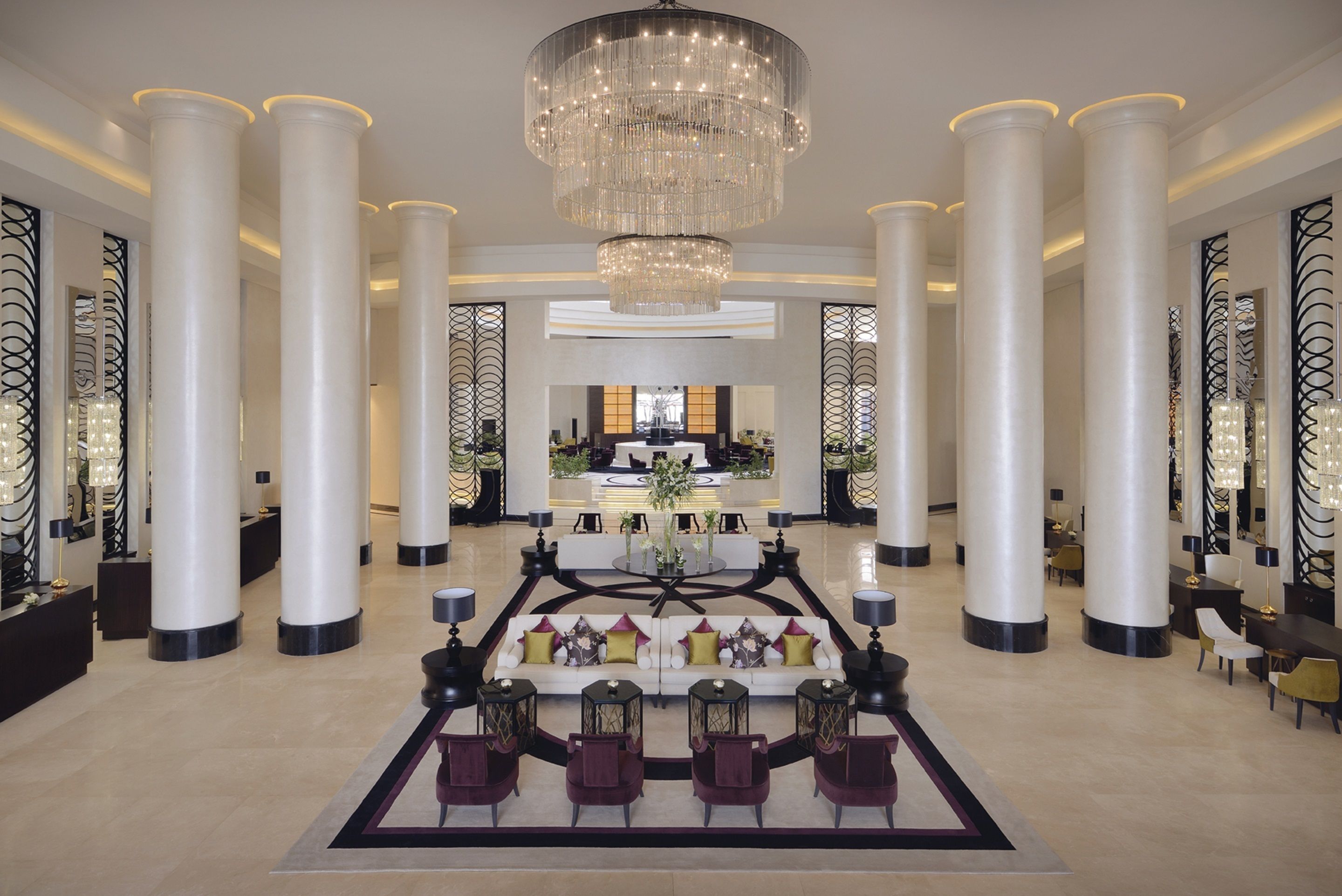 Un hall d’entrée spacieux avec un espace salon central, de grandes colonnes et un lustre.