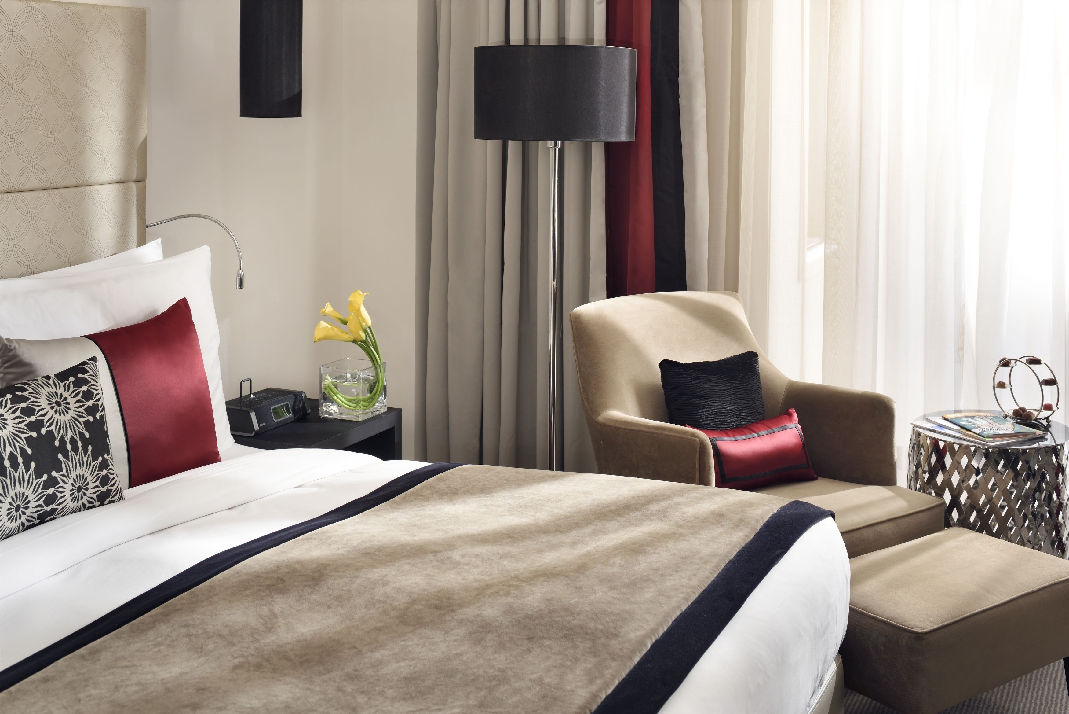 A hotel room with a large bed, a chair, a lamp, and a side table with a vase of flowers.