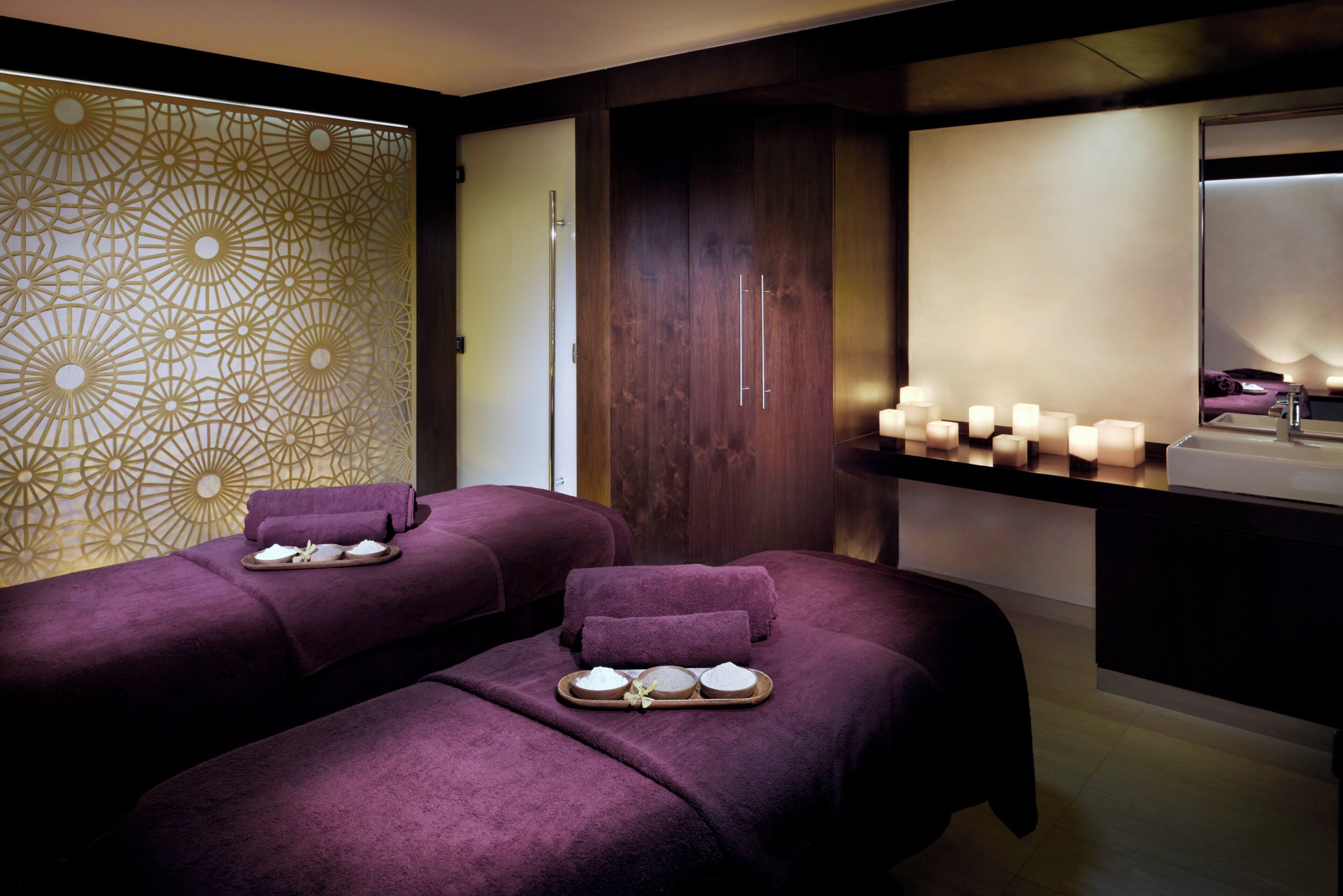 Un cuarto de spa con dos camillas de masaje, una pared decorativa y un tocador con velas.