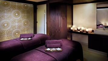 Un cuarto de spa con dos camillas de masaje, una pared decorativa y un tocador con velas.