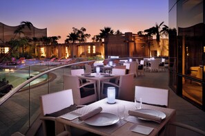 An outdoor dining area with tables and chairs, a pool, and palm trees. - voco Riyadh by IHG (Riyadh)