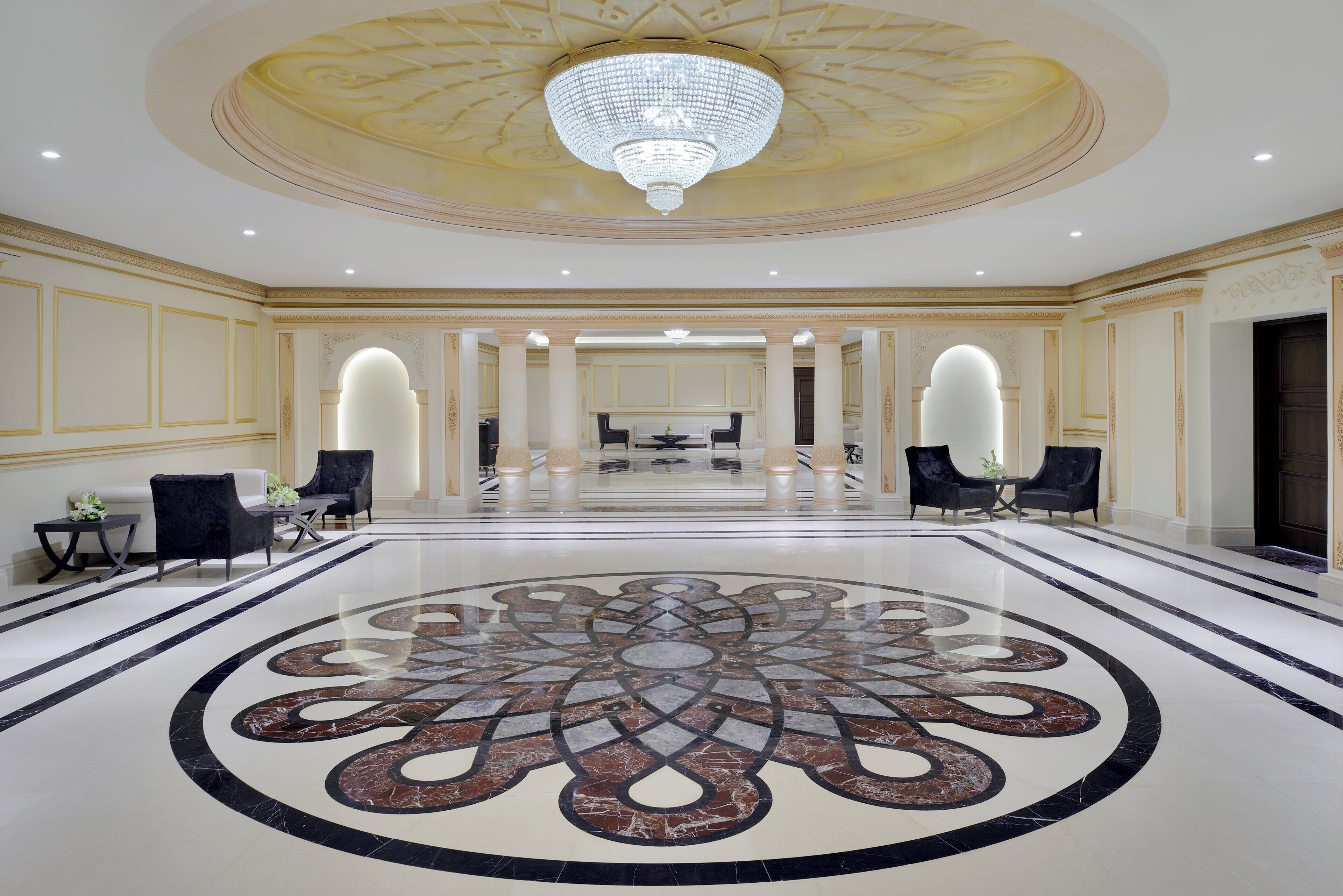 A spacious lobby with a large chandelier, marble flooring, and symmetrical seating arrangement.