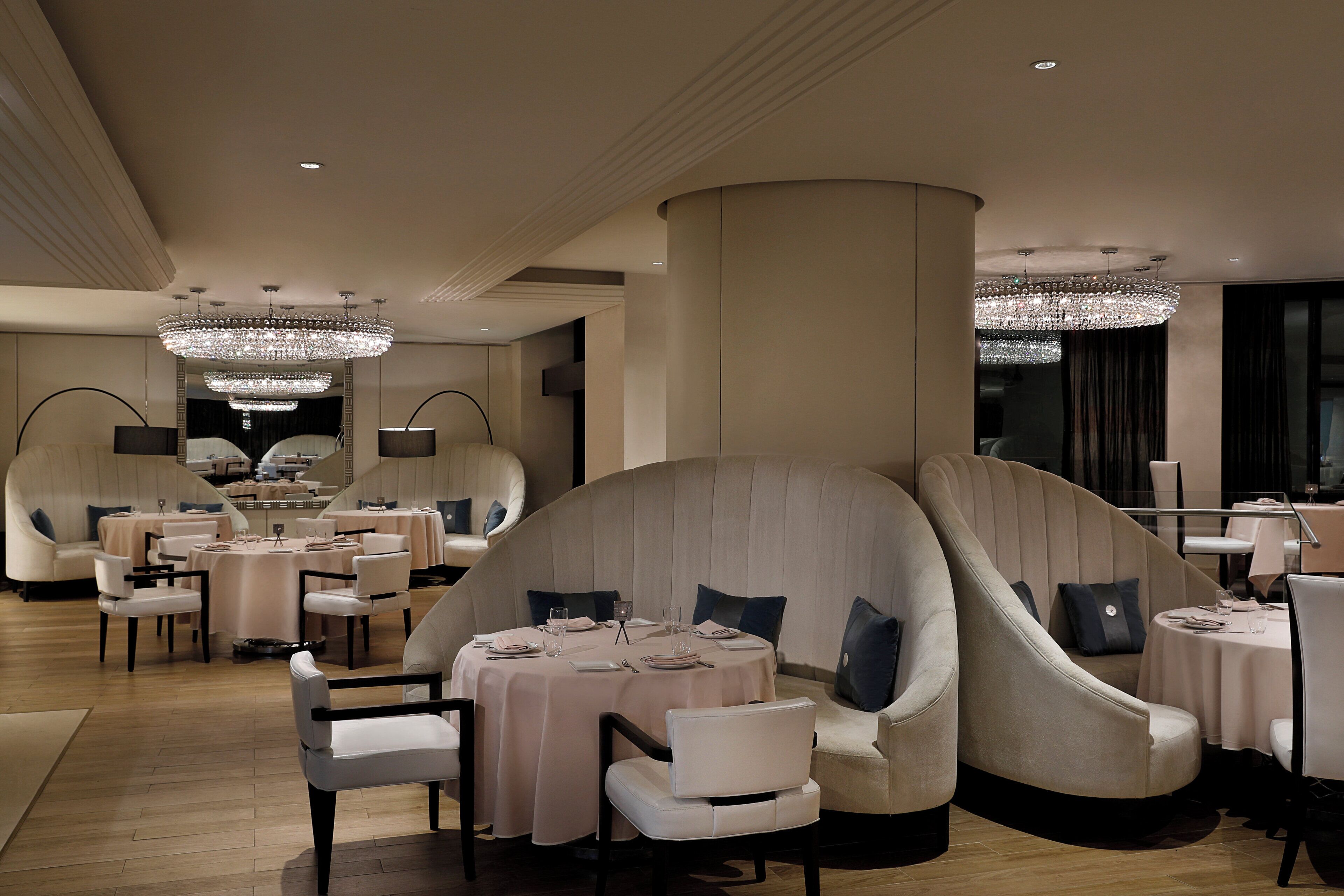 A modern dining area with round tables, cushioned seating, and decorative chandeliers.