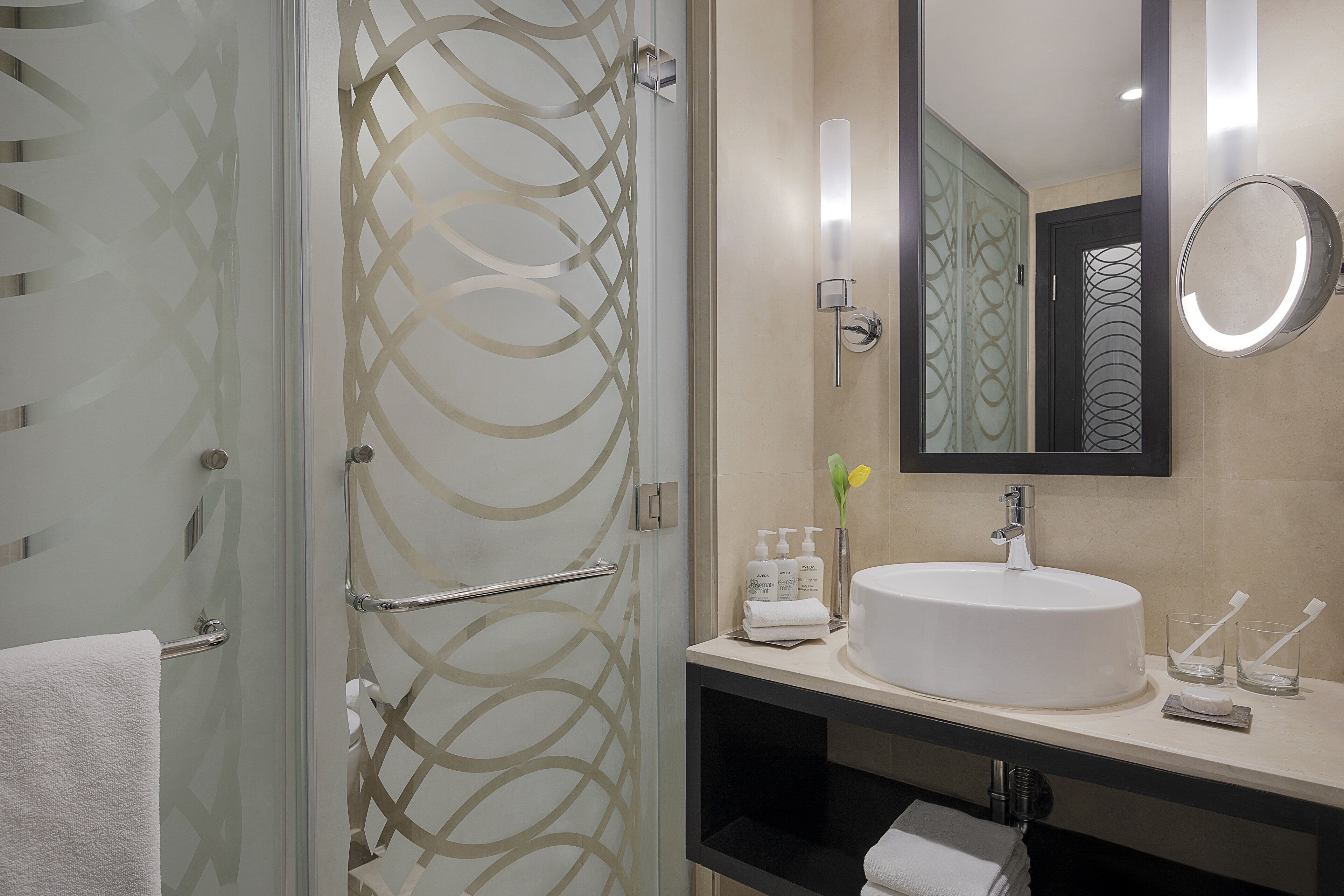 Een moderne badkamer met een douchecabine van glas, een ronde spiegel, een wastafel en toiletartikelen.