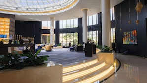 A spacious lobby with a high ceiling and a glass dome, featuring a reception desk, seating areas, and large windows.