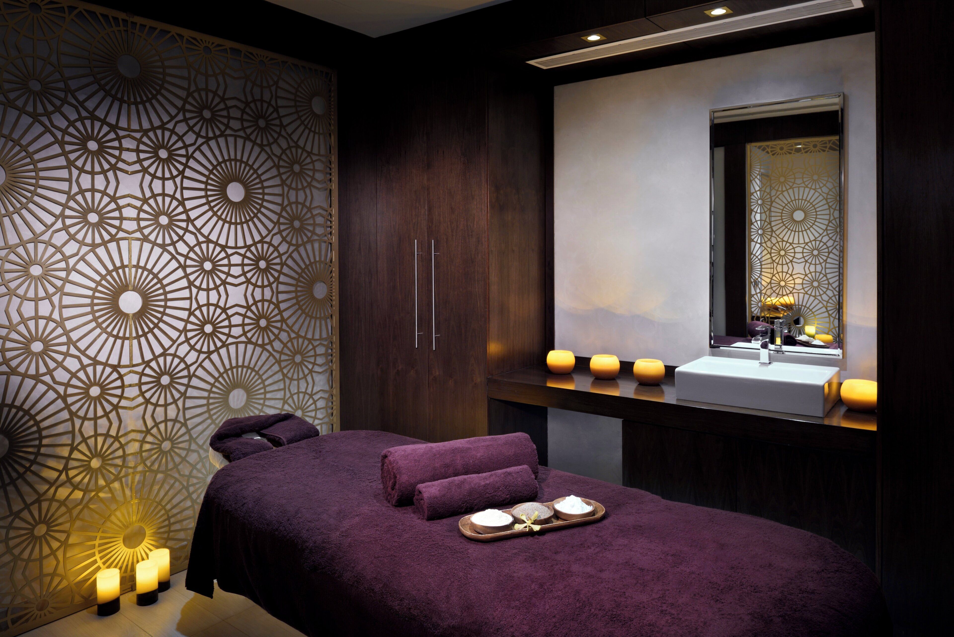 Un cuarto de spa con una cama, un tocador con espejo, velas y una bandeja con productos de baño.
