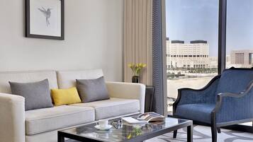 A modern living room with a sofa, armchair, and coffee table, featuring a city view through large windows.