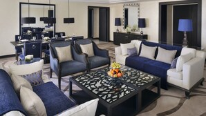 A modern living room with a dining area, featuring a glass coffee table with fruit, sofas with blue and white cushions, and a large mirror above the dining table.