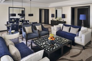 A modern living room with a dining area, featuring a glass coffee table with fruit, sofas with blue and white cushions, and a large mirror above the dining table. - voco Riyadh by IHG (Riyadh)