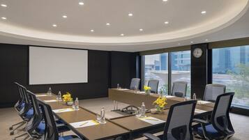 A conference room with a long table, chairs, a projector screen, and a clock on the wall.