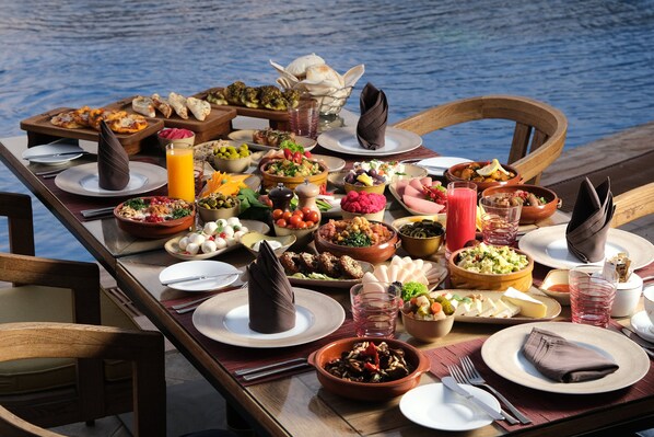 A table set with various dishes and drinks, overlooking a body of water. - voco Riyadh by IHG (Riyadh)