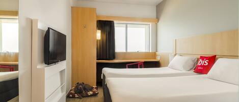 A hotel room with a bed, a desk, a TV, and a window.