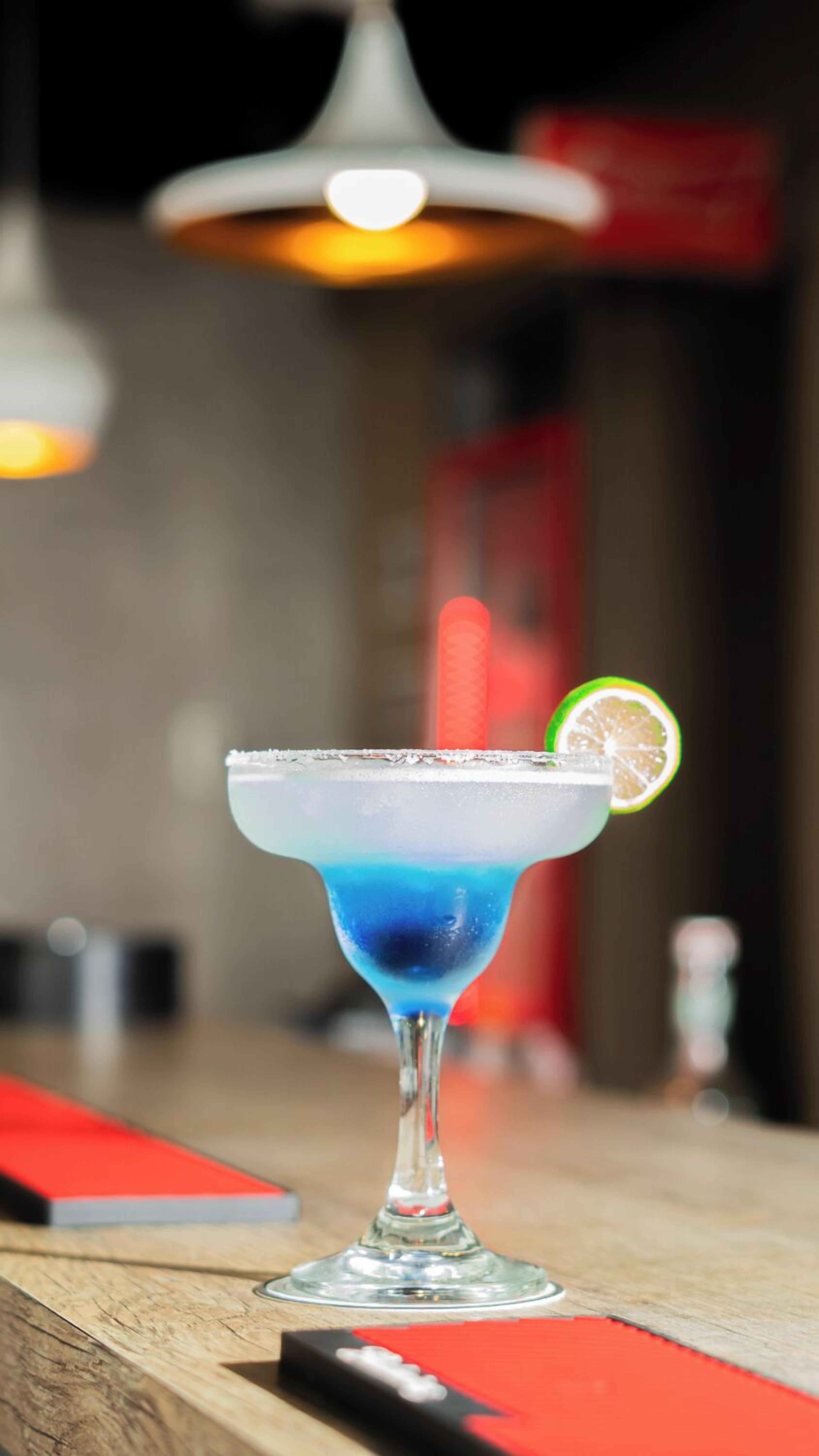 A cocktail with a blue liquid and a lime slice on the rim, served in a glass with a salted rim.