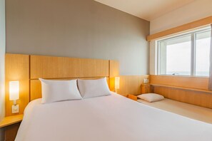 Quarto de hotel com uma cama grande, duas mesas de cabeceira, uma janela e cabeceira de madeira.