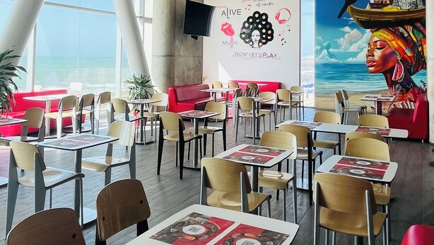 Un restaurant avec de hauts plafonds, des luminaires suspendus et une fresque murale. Les tables et les chaises sont disposées pour accueillir les clients.