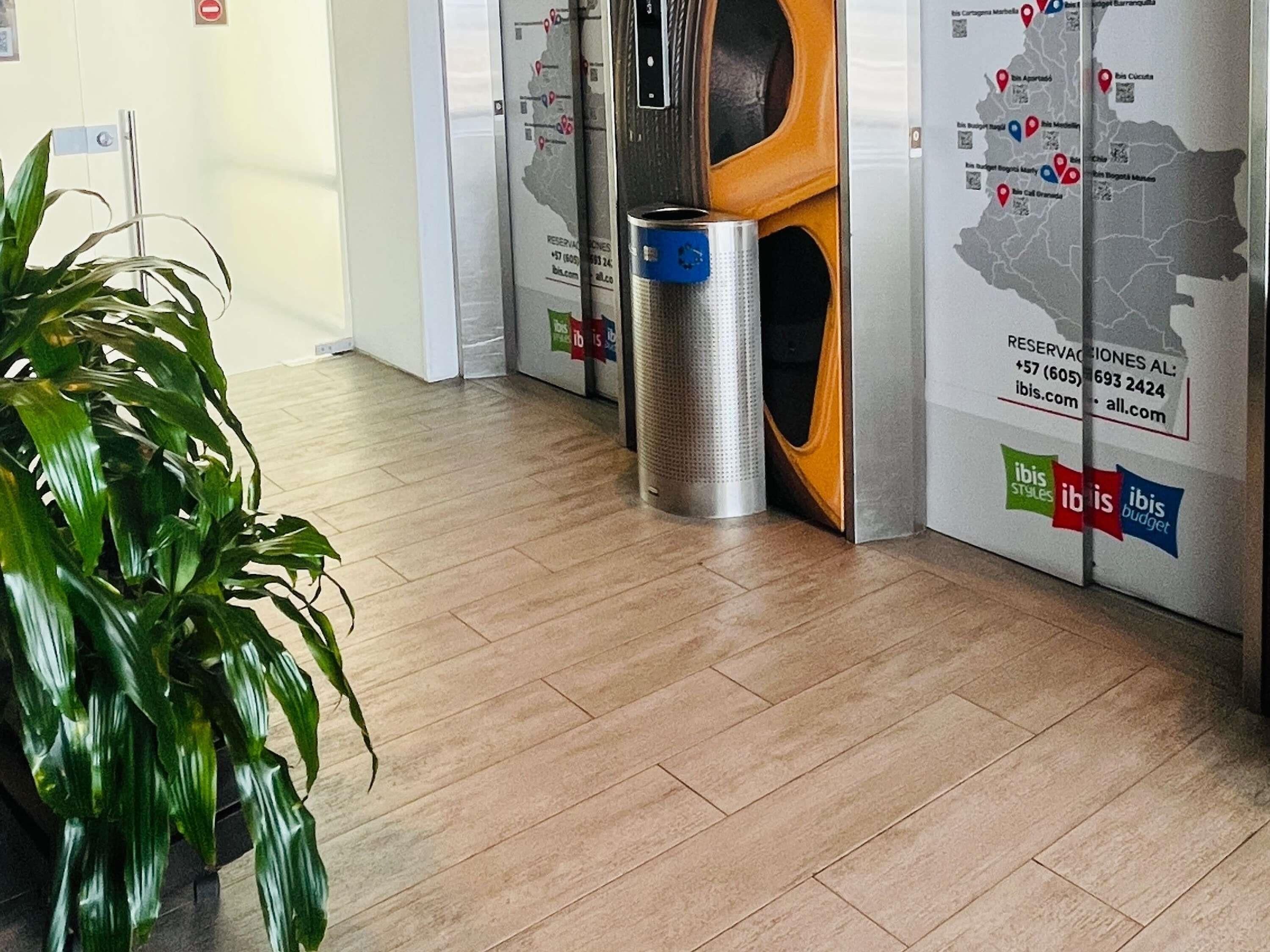 A hotel lobby with a wooden floor, a trash bin, and a wall with a map and contact information.