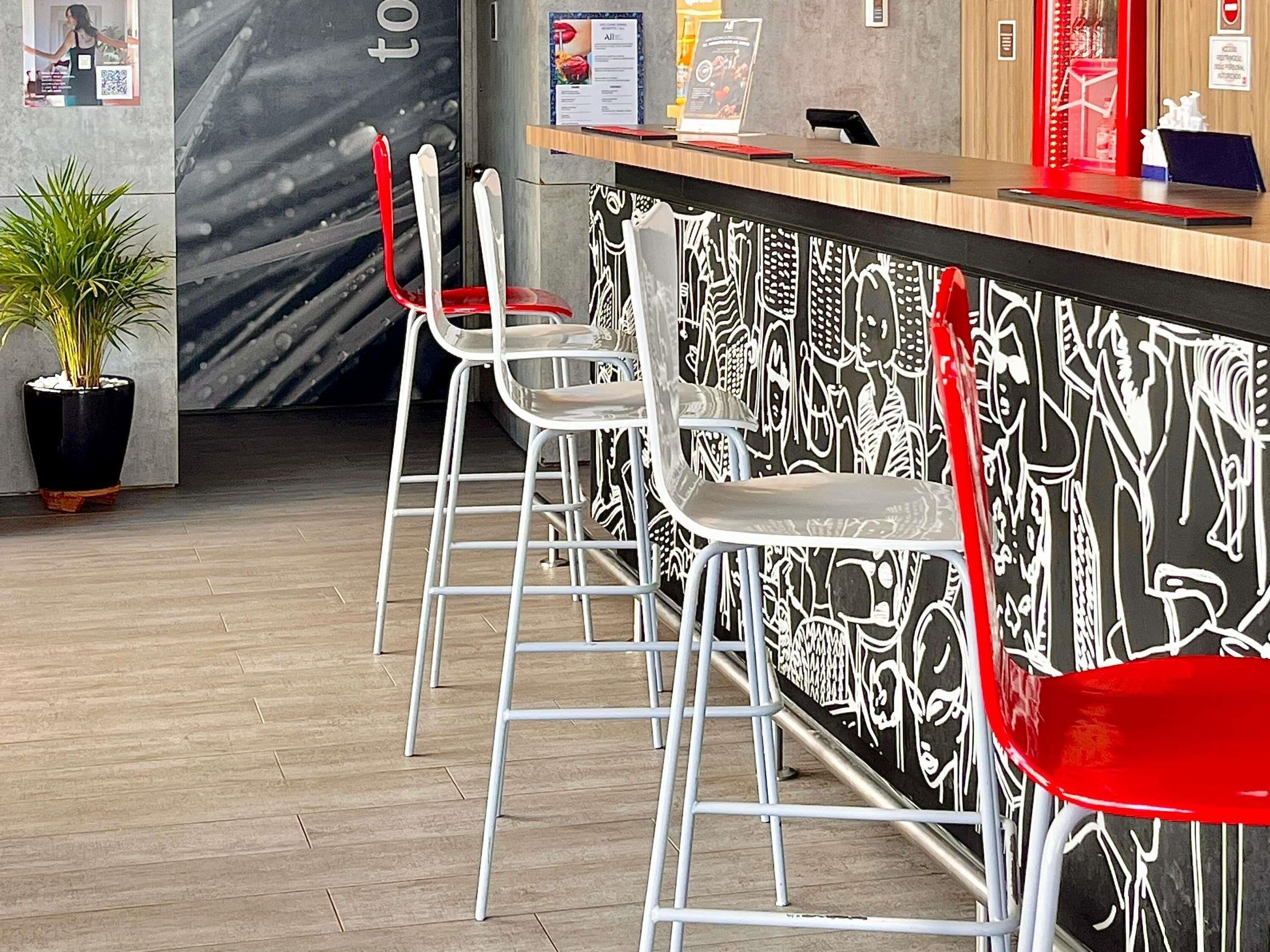 Zona de bar con mostrador, sillas blancas y rojas, y pared con diseño.