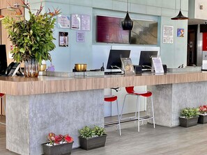 Um balcão de recepção com design moderno, uma grande planta em vaso e uma área de estar com cadeiras vermelhas.