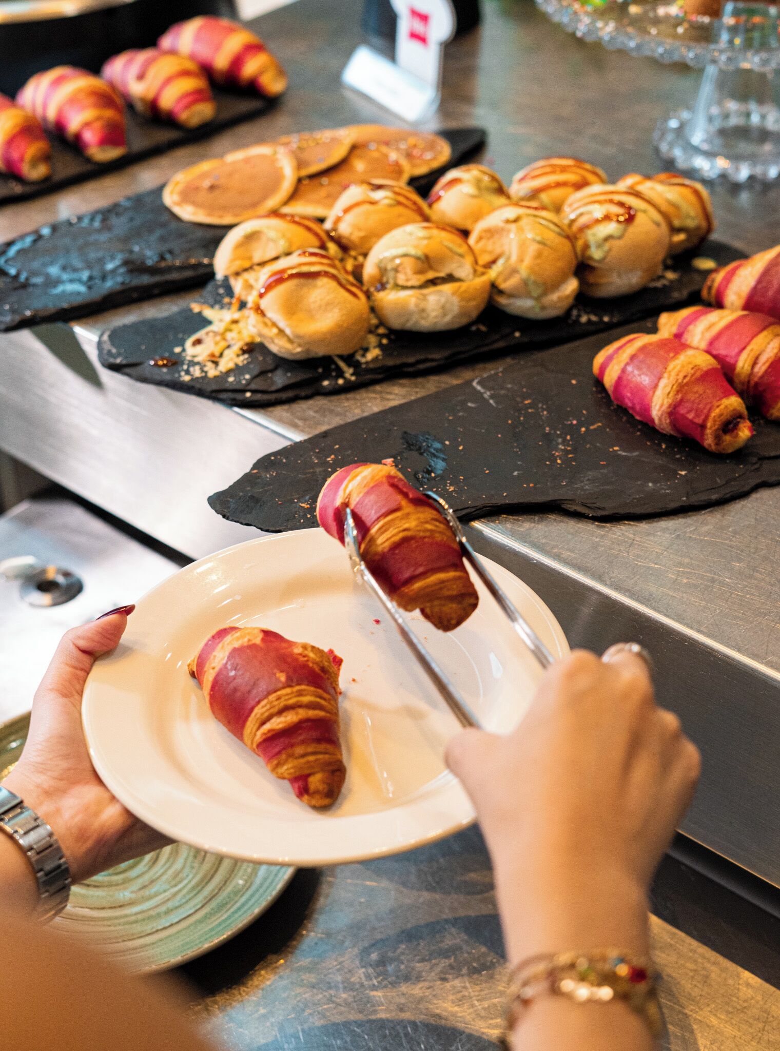 A person holding a plate with a croissant wrapped in bacon.