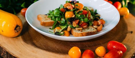 A plate of food on a wooden board with a yellow squash and cherry tomatoes around it.