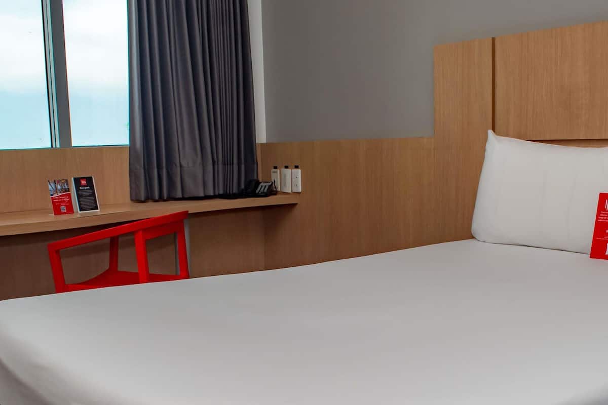 Et hotelværelse med en seng, et skrivebord med telefon og et vindue med gardiner.