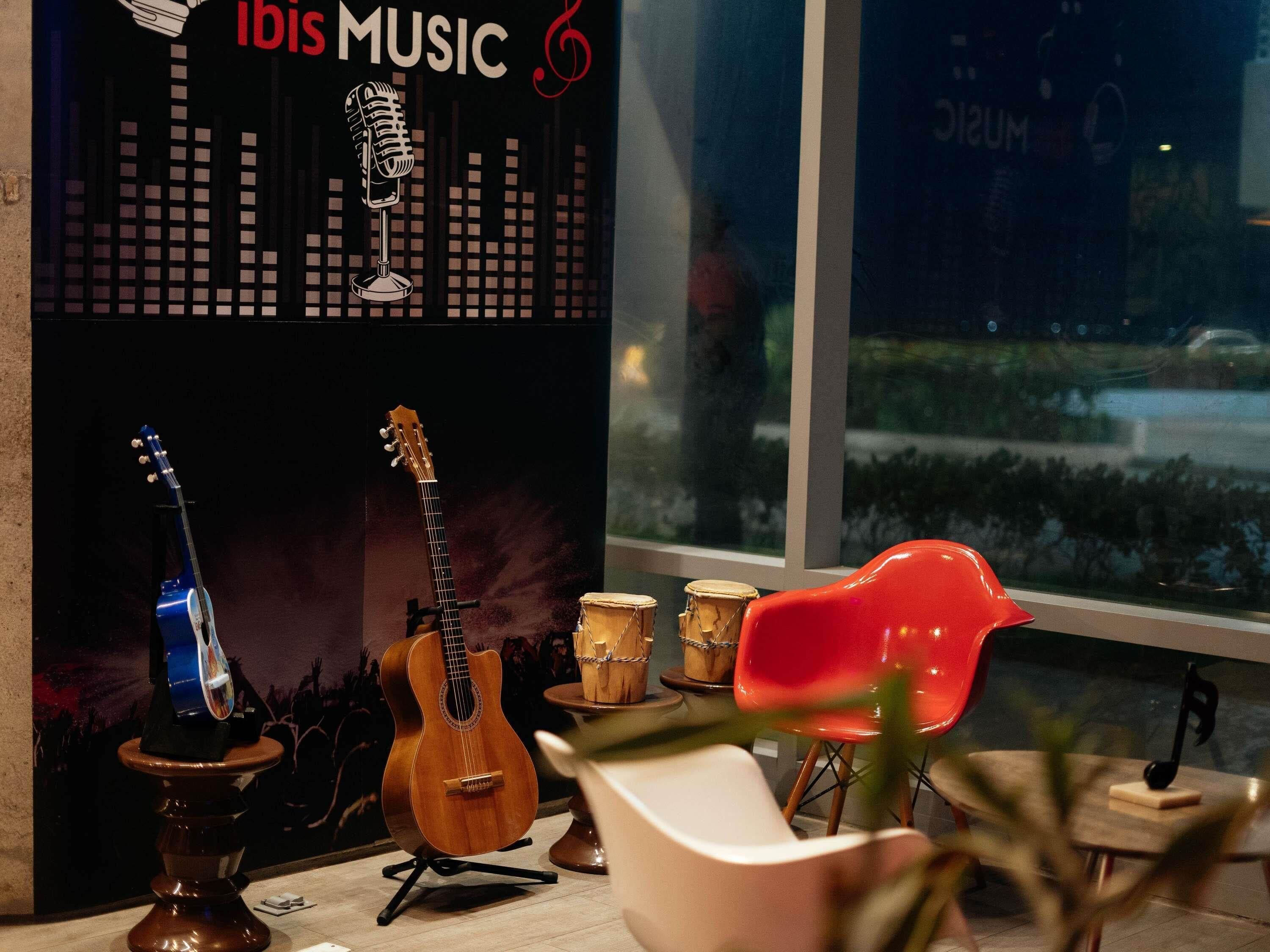 A room with a guitar, a red chair, and a poster with 'IBIS MUSIC' text.