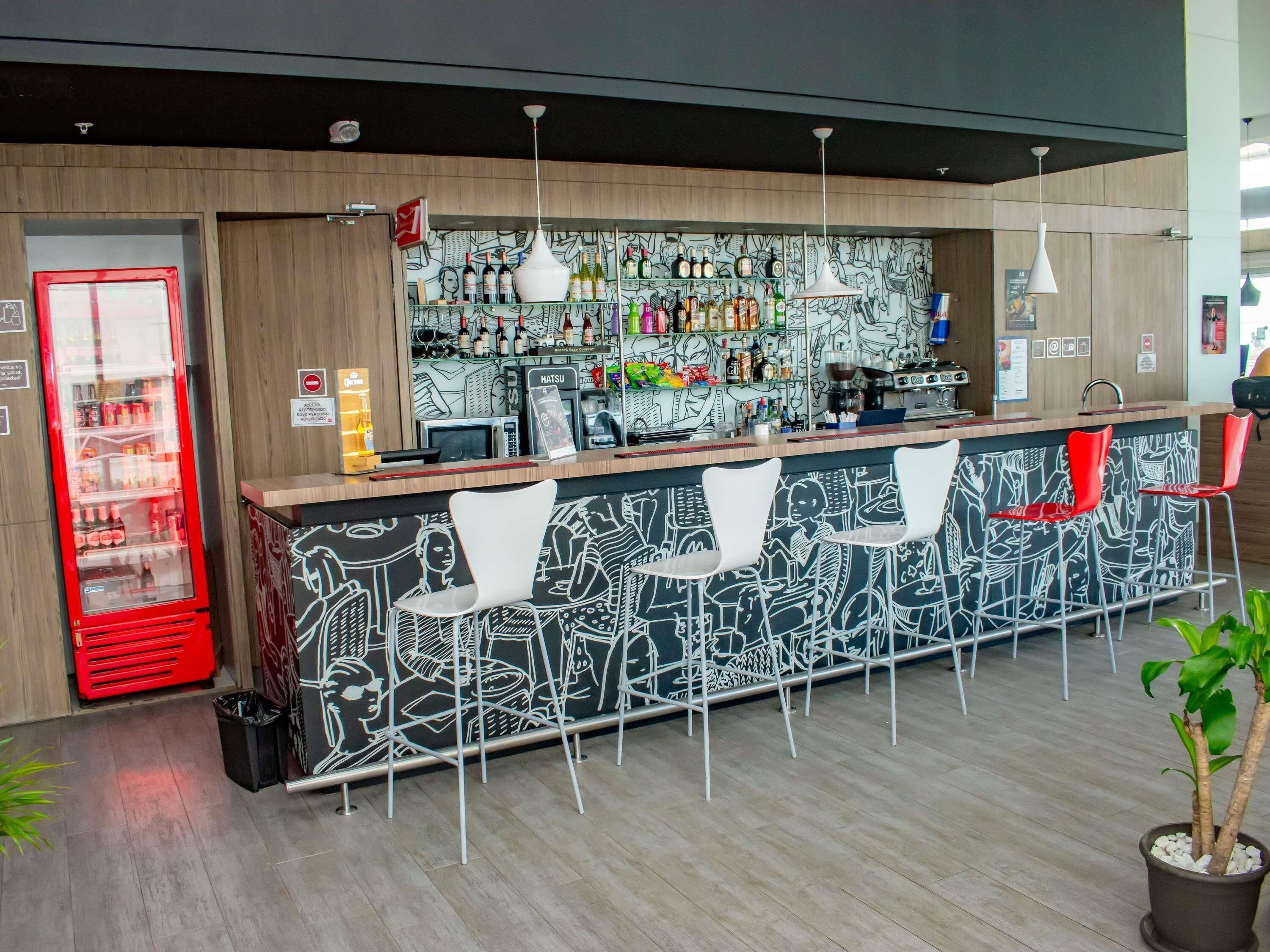 A bar area with a counter, bar stools, a refrigerator, and a wall with a mural.