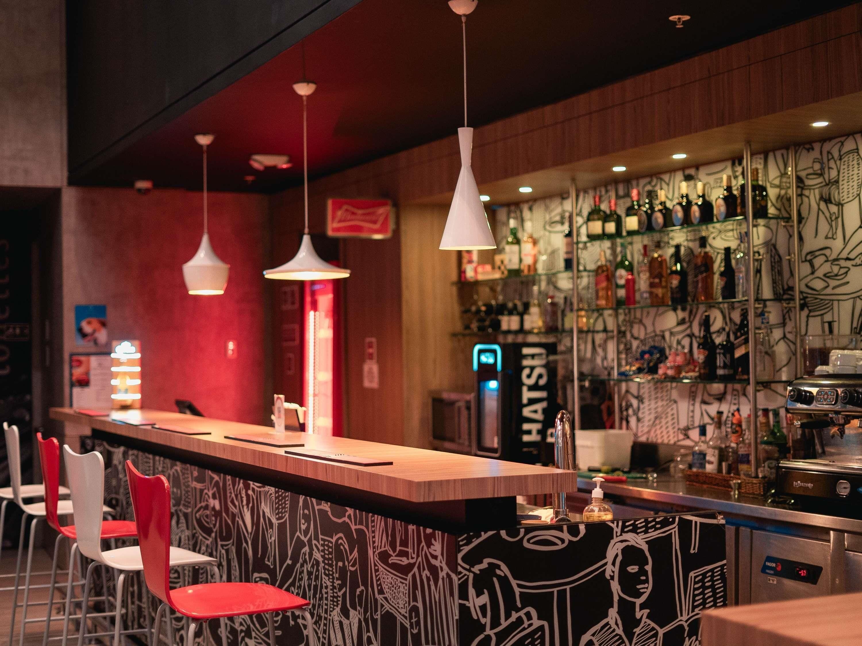 Zona de bar con mostrador, sillas rojas, lámparas colgantes y un muro con grafitis.
