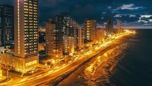 Un paisaje urbano costero nocturno con edificios iluminados y una playa.