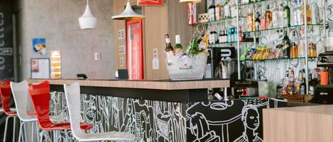 A bar area with a counter, ice bucket, and a variety of bottles. There are red and white chairs and a wall with a black and white mural.