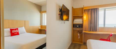 Une chambre d’hôtel avec deux lits, une télévision, un bureau et une fenêtre avec des rideaux.