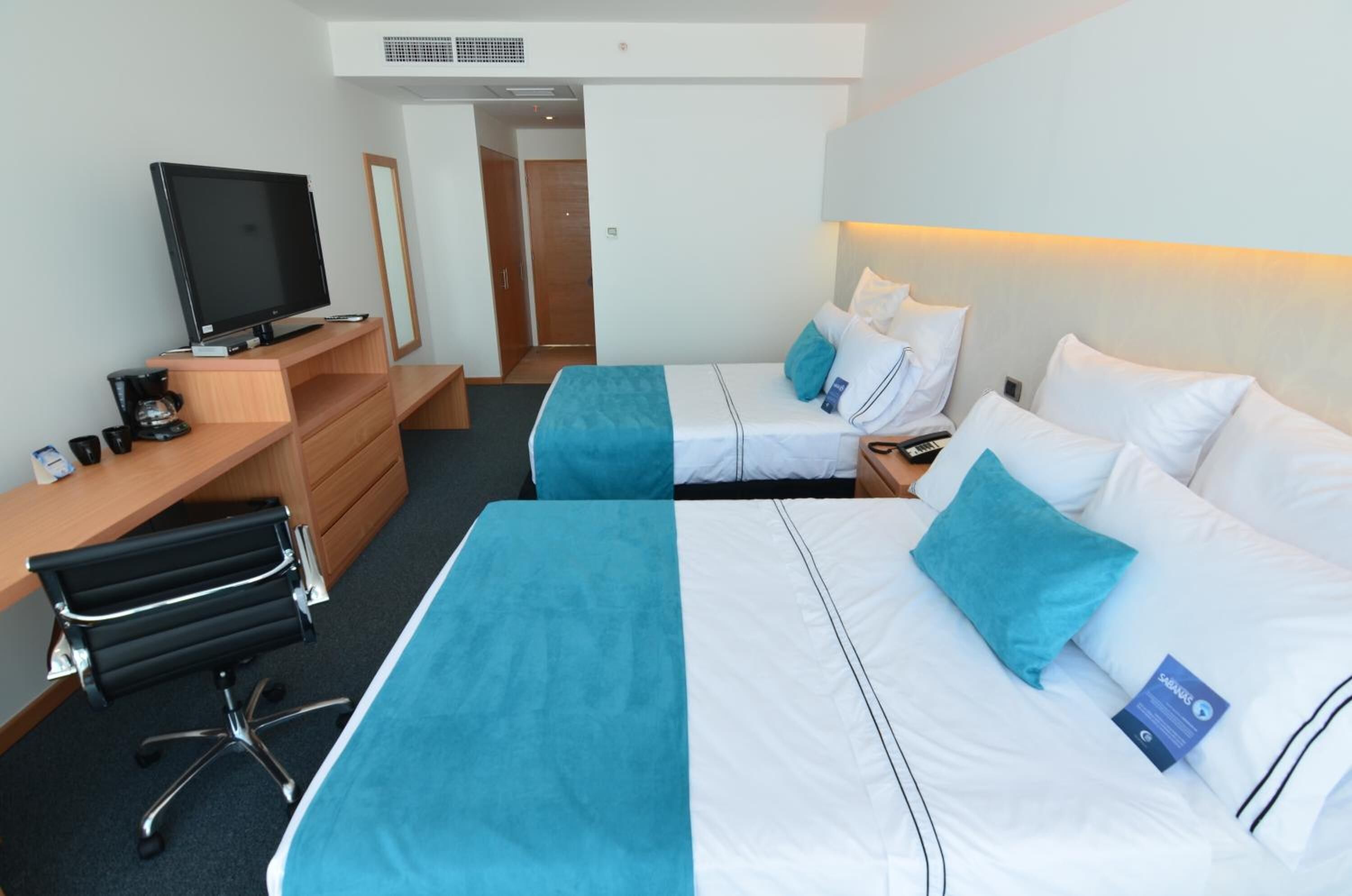 A hotel room with two beds, a desk with a computer, a TV, and a chair.