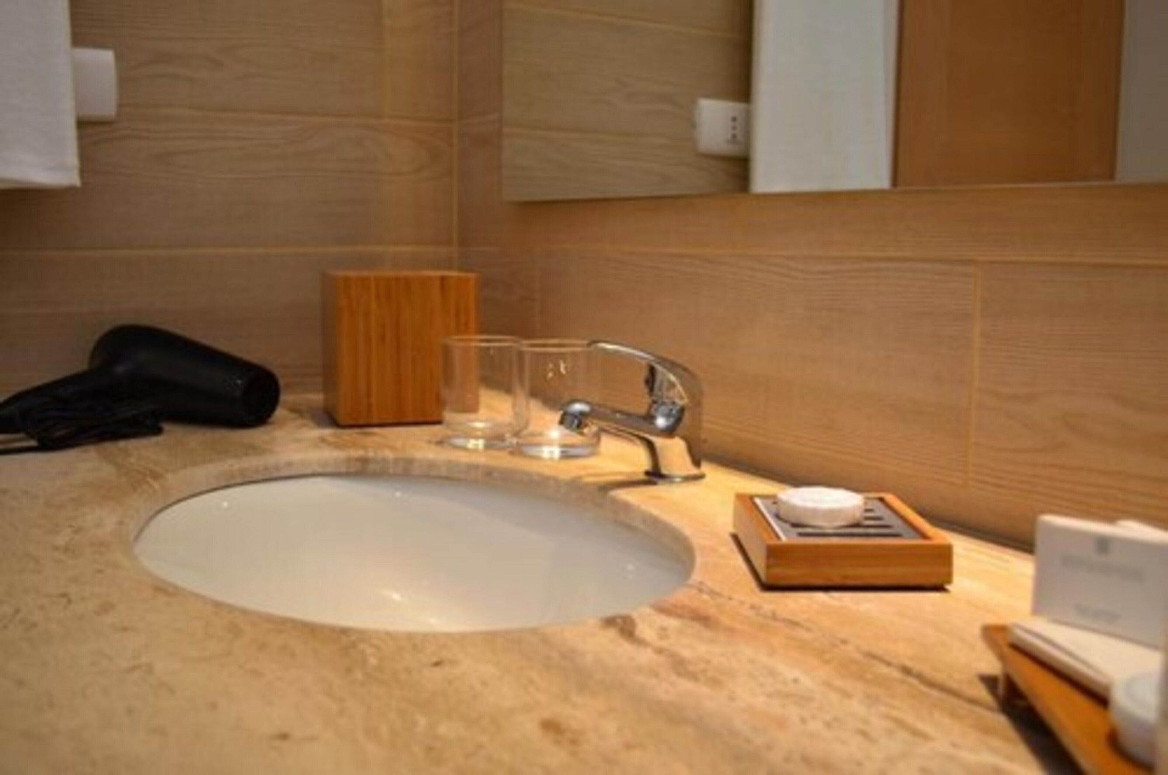 Une salle de bain avec un lavabo rond, un meuble en bois et un récipient en verre posé sur le comptoir.